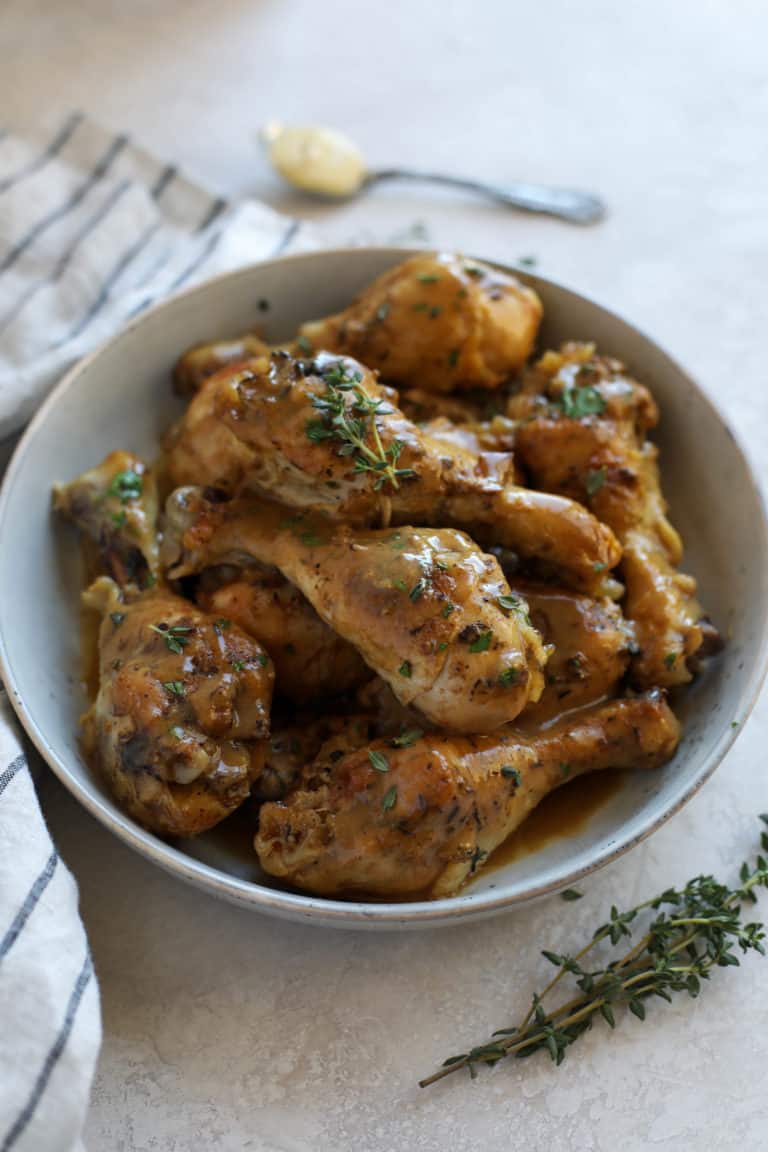 Dijon-thyme chicken legs piled into a white serving bowl.