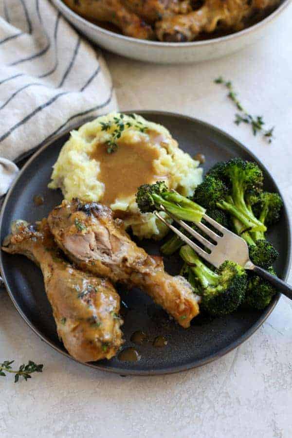 Overhead close view of a plate of chicken wings, mashed potatoes & gravy, and broccoli with a piece of broccoli on a fork lifted towards the camera