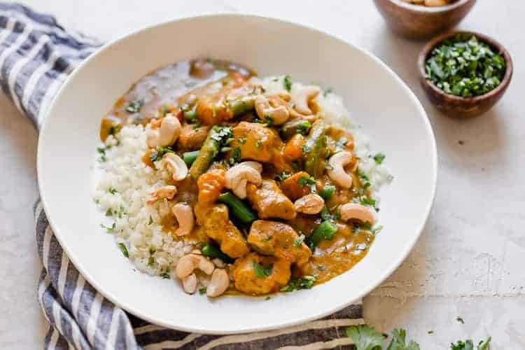 White bowl with serving of slow cooker sweet potato chicken curry topped with cashews