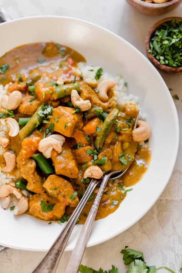 Overhead shot of Slow Cooker Sweet Potato Chicken Curry in a white bowl served over cauliflower rice with two spoons.