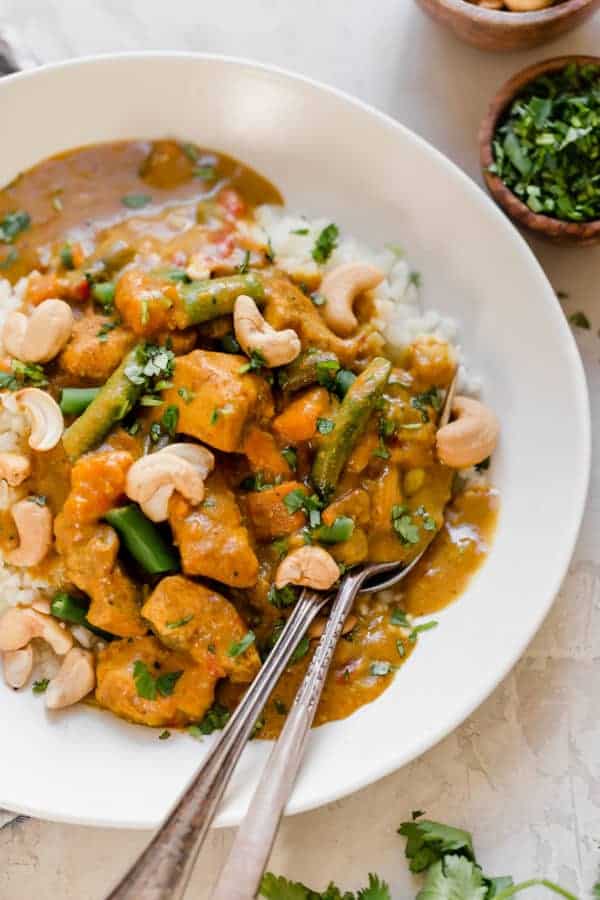 Close up view of Slow Cooker Sweet Potato Chicken Curry in a white bowl topped with cashews and fresh herbs. 