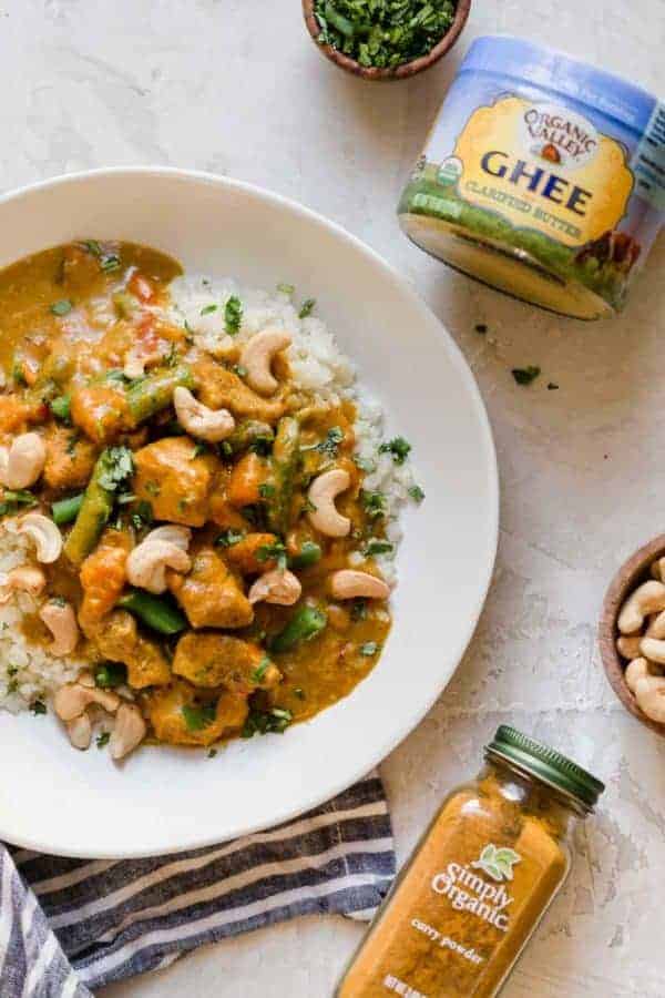 Overhead shot of Slow Cooker Sweet Potato Chicken Curry in a white bowl served over cauliflower rice with a jar of Organic Valley Ghee and Simply Organic Curry Powder laying next to it.