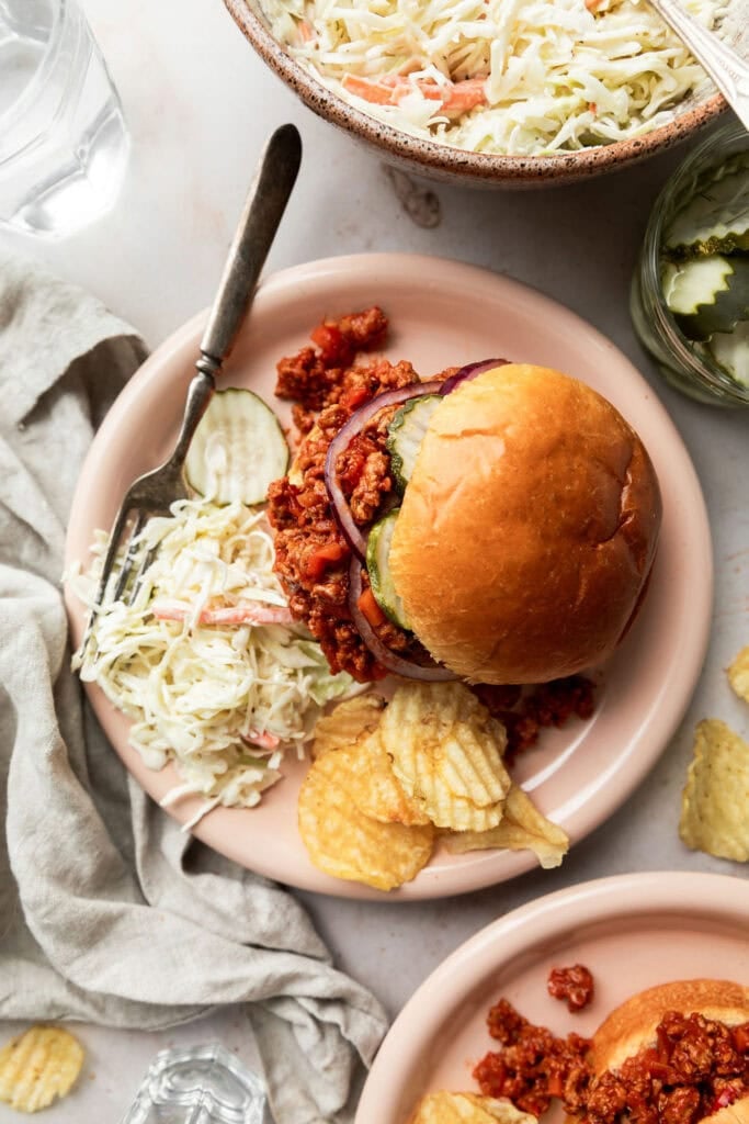 Overhead view of a plate with a ground turkey sloppy joe, fresh cole slaw, and crispy potato chips. 