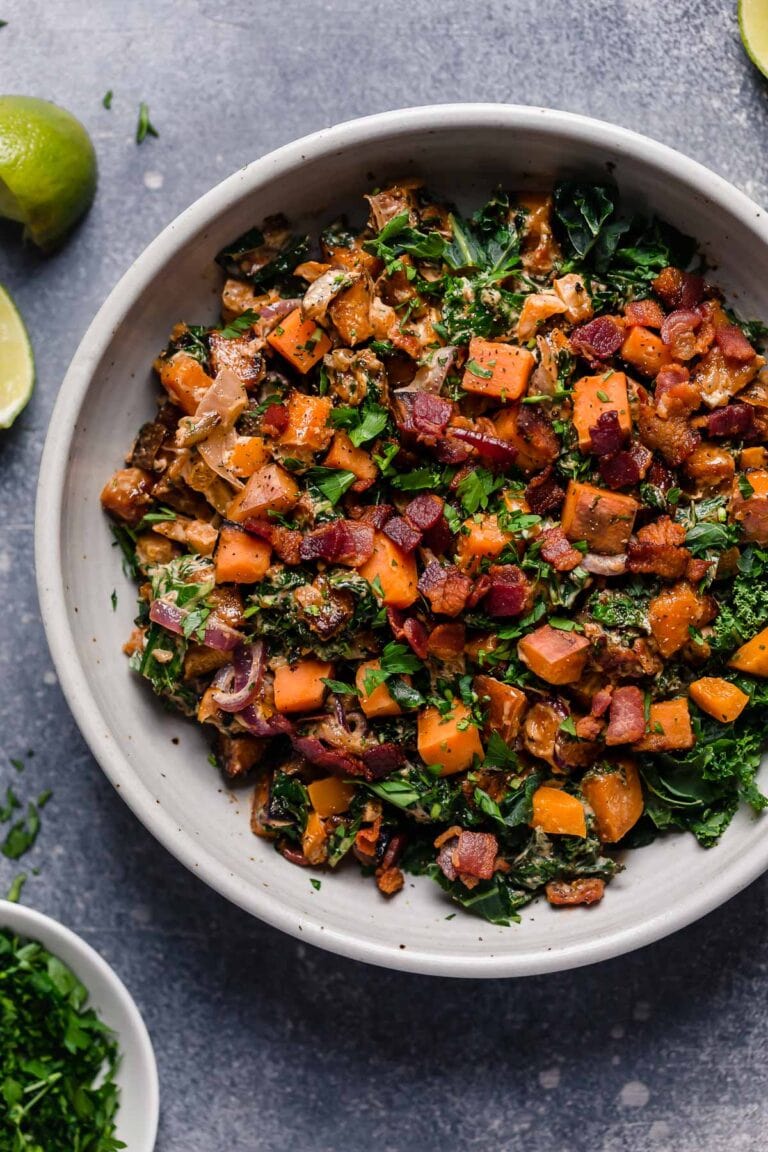 A large bowl of warm kale salad with crispy bacon pieces and lime dressing. 