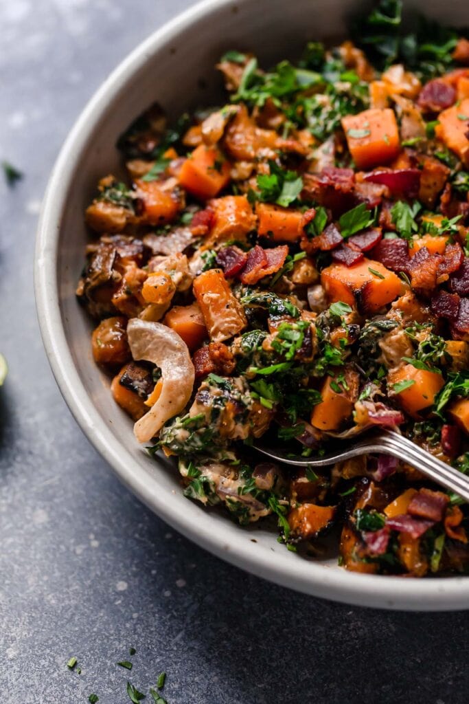  A side view of Warm Chipotle Lime Sweet Potato Salad in a light gray serving bowl garnished with cilantro. 