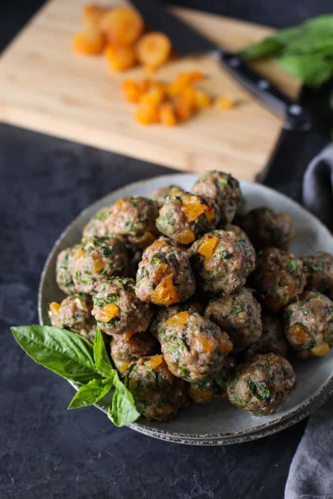 Bowl of Apricot Basil Breakfast Meatballs with a cutting board, knife and dried apricots. 