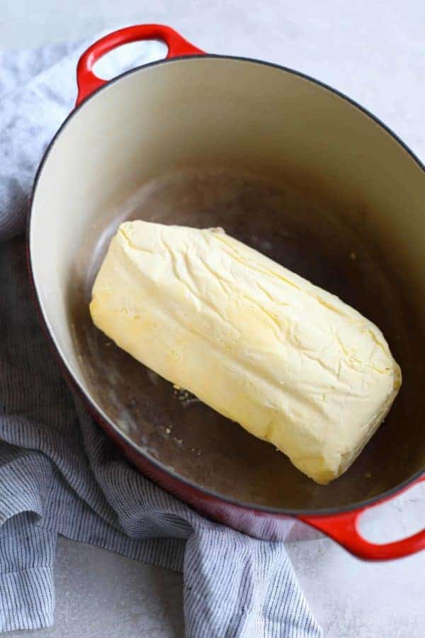 A red Dutch oven with a large hunk of butter in the bottom. 