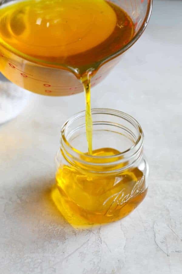 Pouring liquid ghee from measuring cup into a glass jar. 