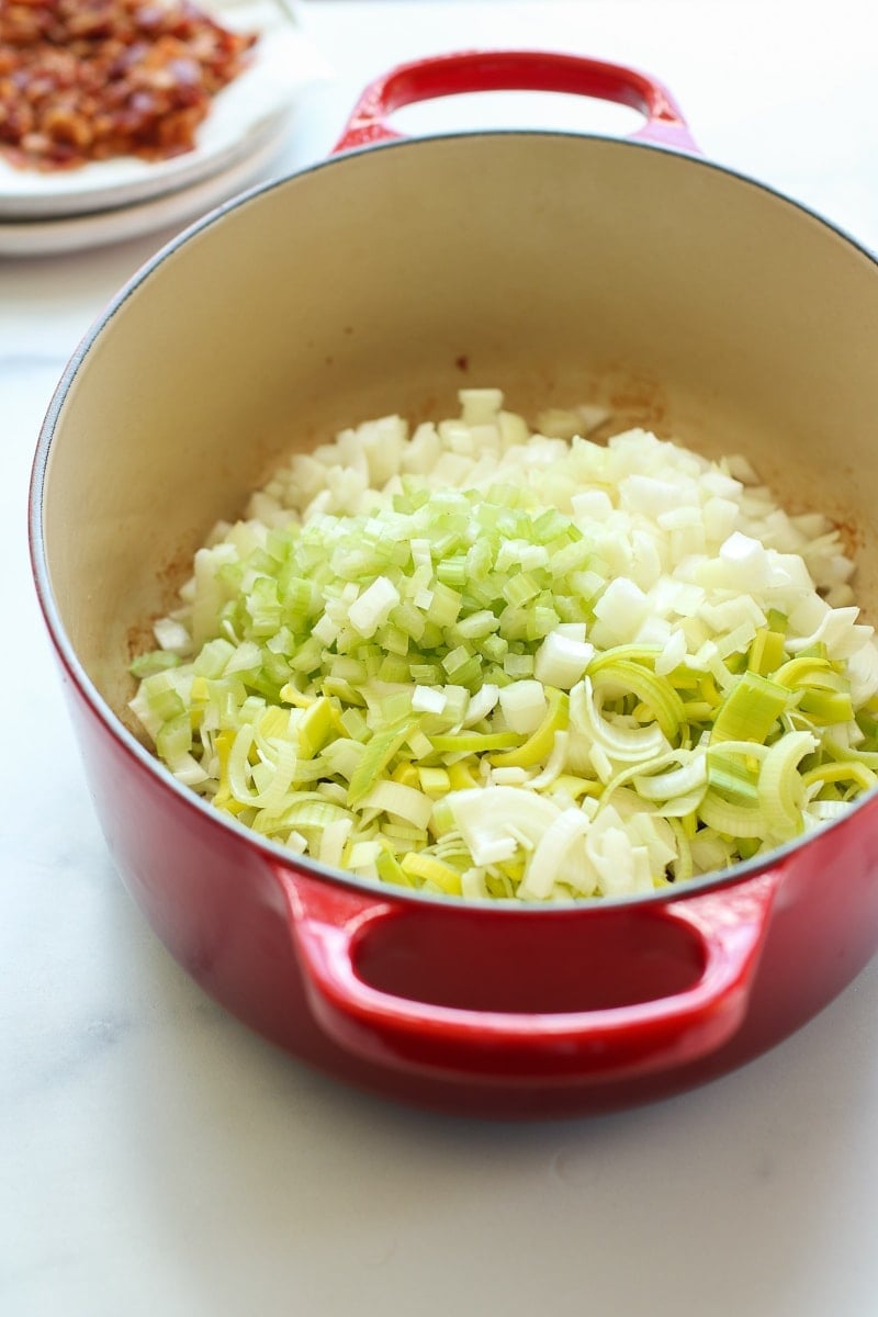 A red saucepan filled with ingredients for potato leek soup