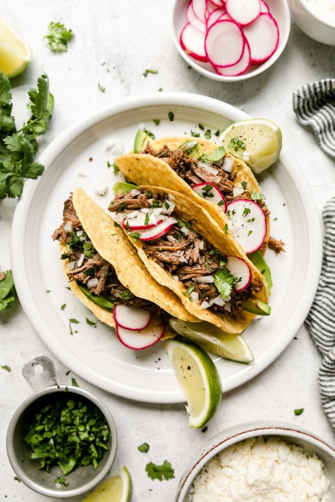 White plate with three hard shell tacos filled with slow cooker beef barbacoa and fresh cilantro.
