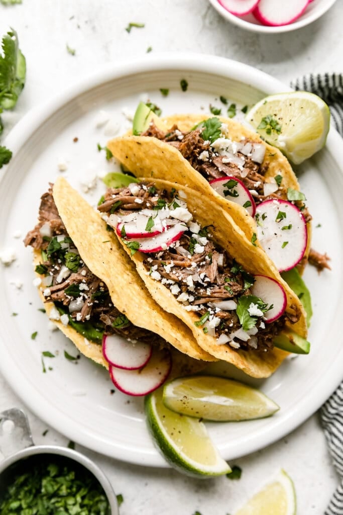 Three hard shell tacos filled with slow cooker beef barbacoa with sprinkle of fresh cilantro, radishes, and riced cauliflower.