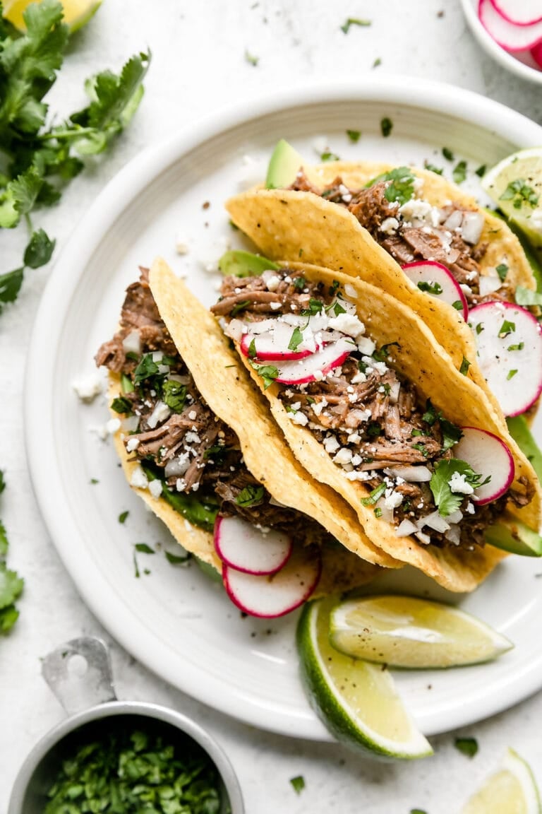 Three hard shell tacos stuffed with slow cooker beef barbacoa and topped with fresh herbs, cheese, and thinly sliced radishes. Served with Lime wedges. 