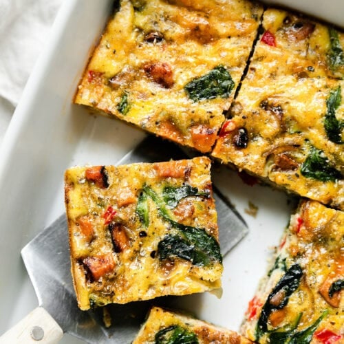 Sweet potato breakfast casserole in white baking dish cut into squares, one serving being removed.