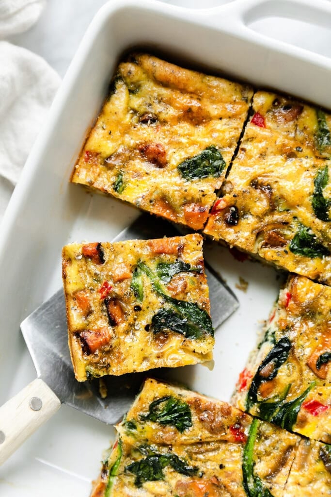 Overhead view sweet potato breakfast casserole in white dish cut into squares, one square being lifted out