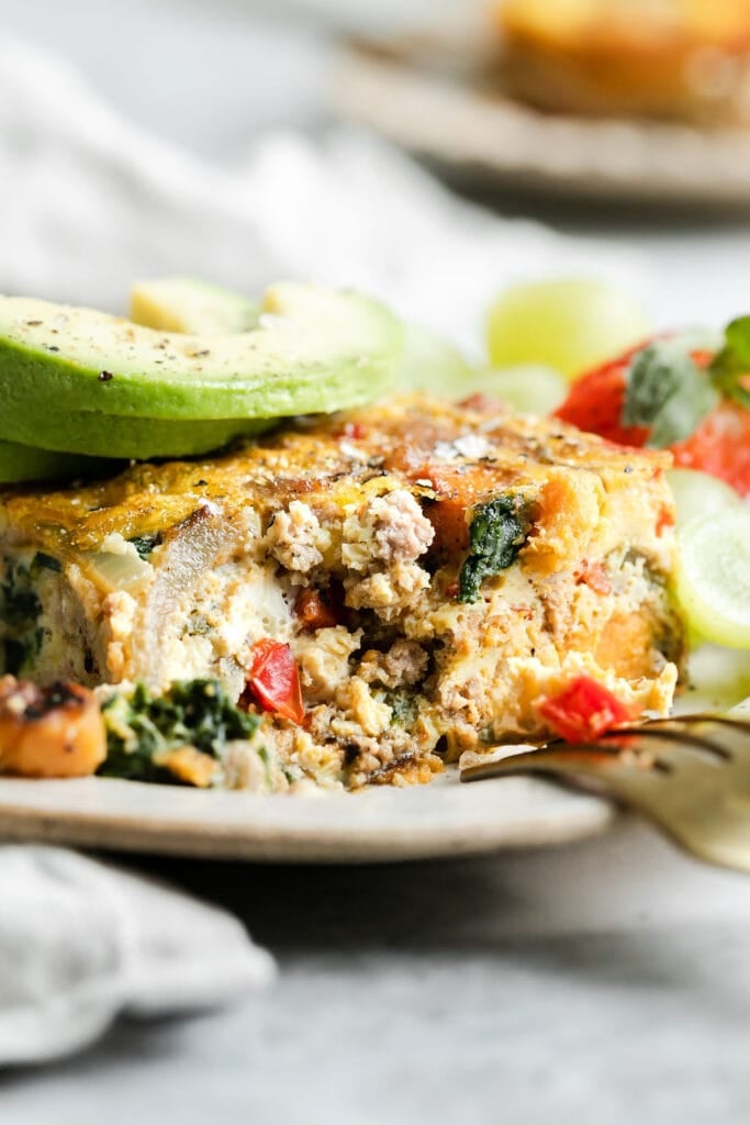 Side view serving of sweet potato breakfast casserole on plate topped with avocado slices.