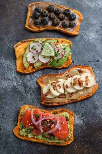 Four slices of oven-baked sweet potato toast shown with nut butter and blueberries, avocado and radishes, nut butter + banana + bacon, and avocado with smoked salmon. 