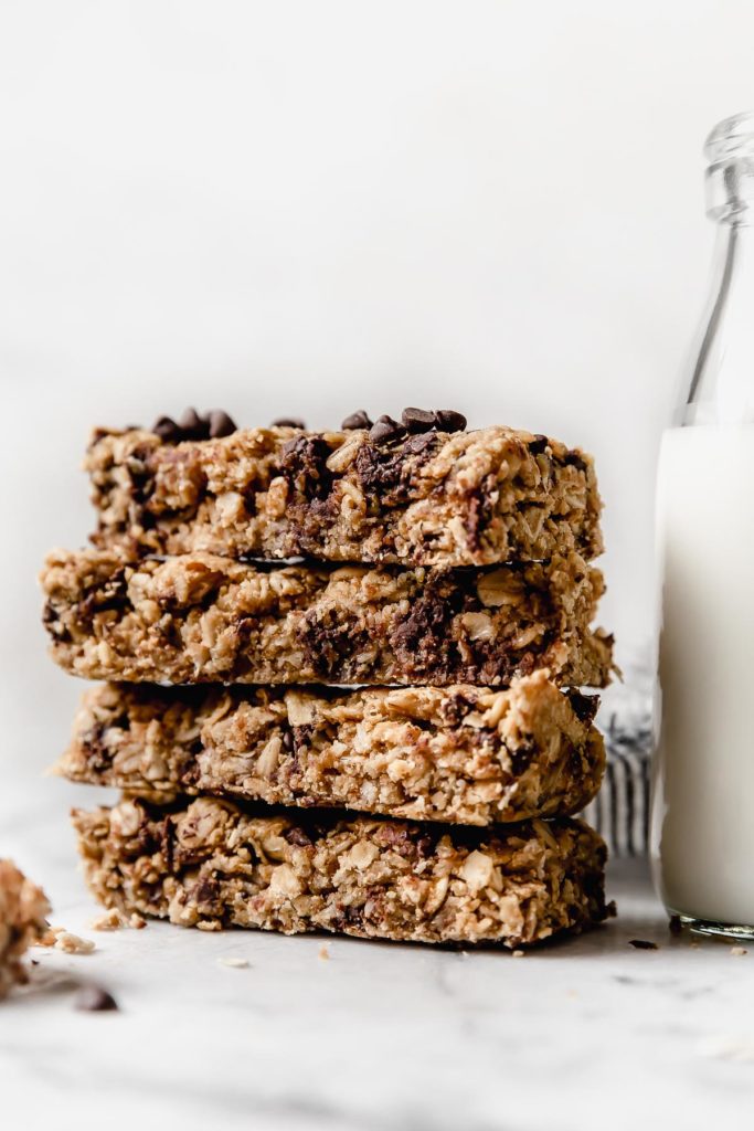 Peanut Butter Granola Bars with chocolate chips stacked vertically next to pitcher of milk