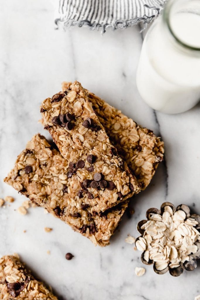 Overhead shot of healthy granola bars, with oats scattered and a glass of milk