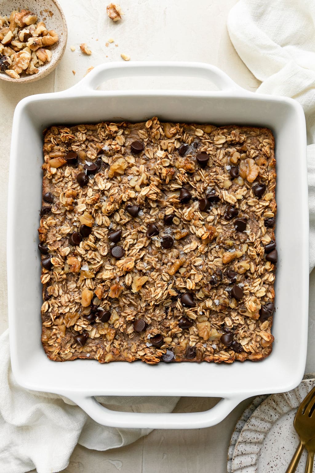 Banana baked oatmeal in a white baking dish topped with chocolate chips and walnuts. 