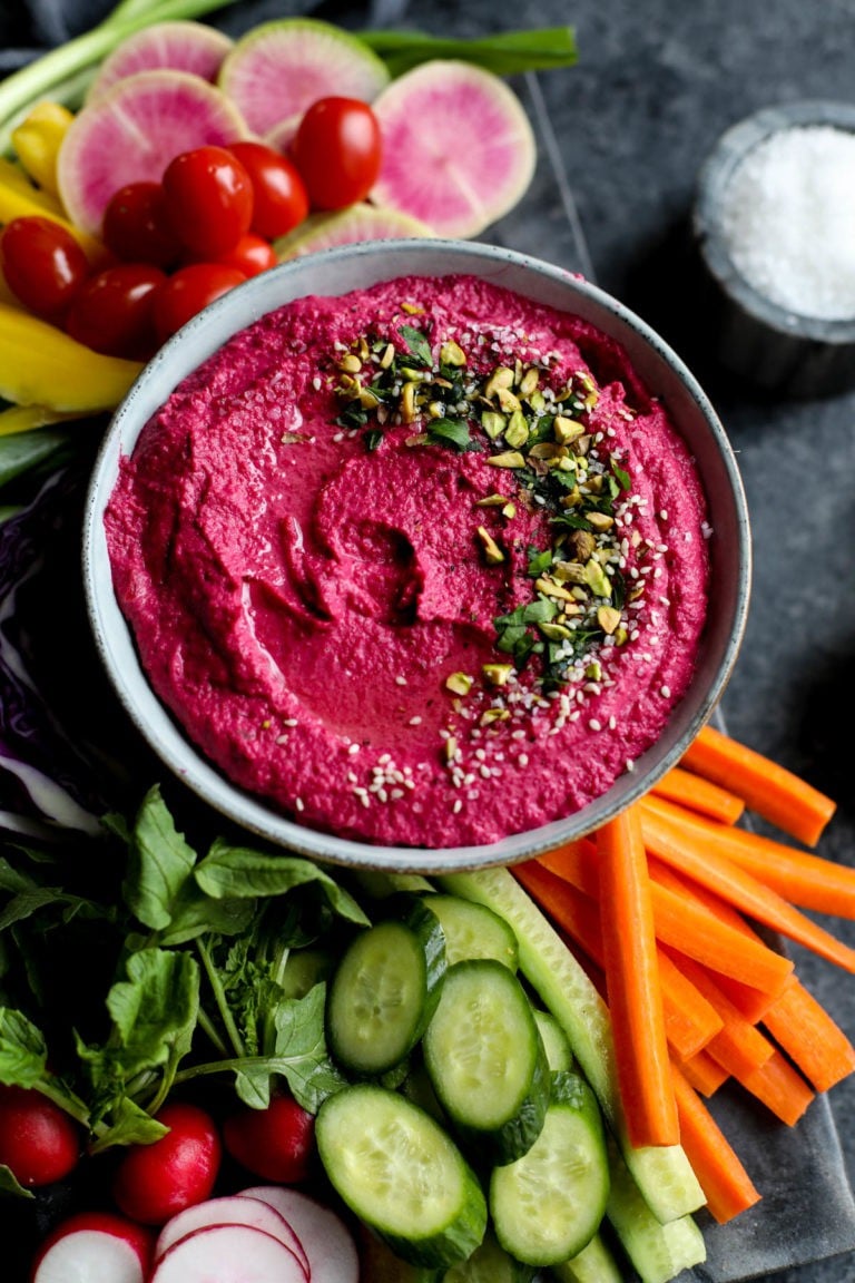 Deep pink beet hummus dip in a bowl on a tray of fresh cut veggies