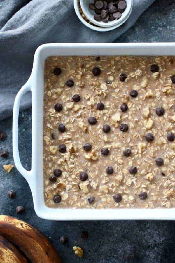 Overhead photo of Banana Chocolate Chip Baked Oatmeal batter in a 9x9 white baking dish reading to go in the oven.