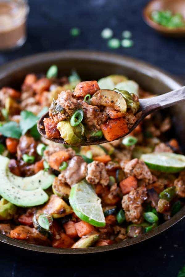 Photo of BBQ Ranch Turkey Veggie Skillet in a cast-iron topped with lime wedges, avocado, cilantro and green onion.