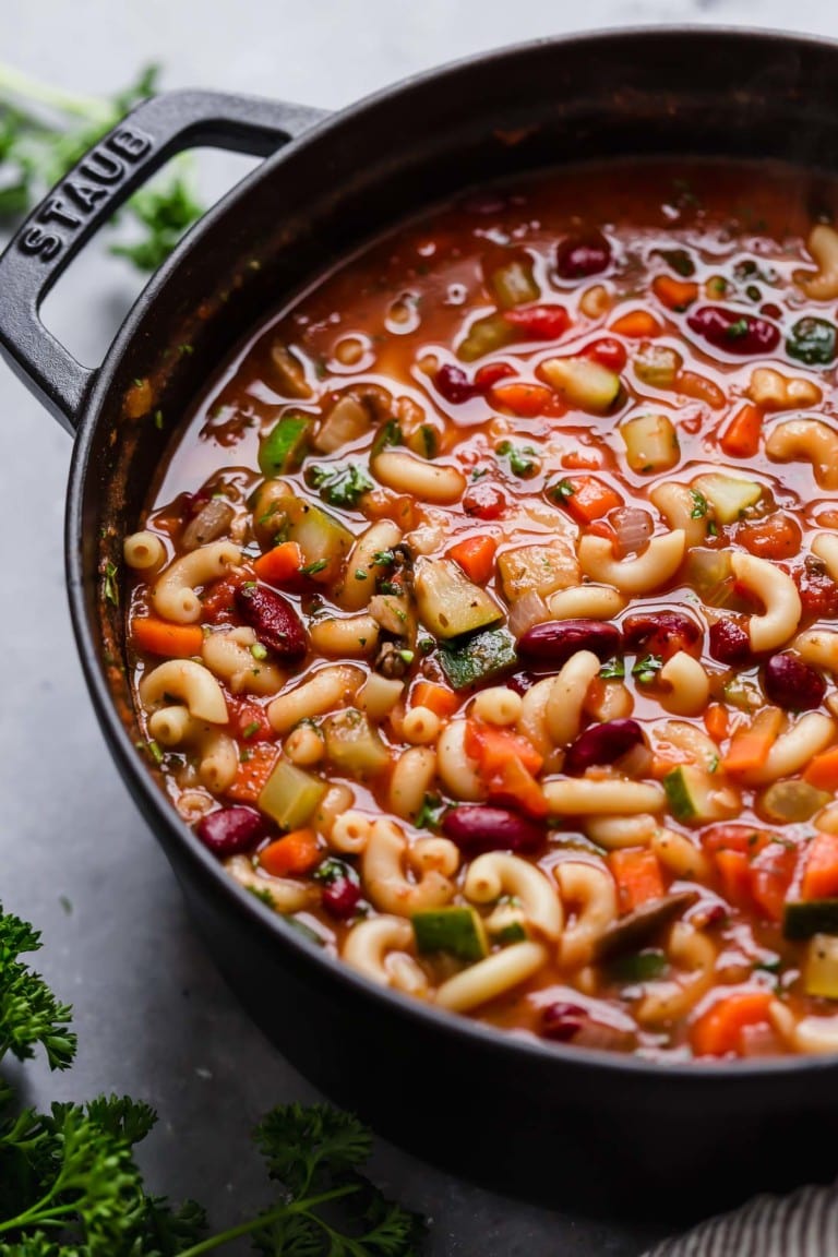 A cast iron Dutch oven with a Minestrone Soup full of beans and macaroni noodles. 