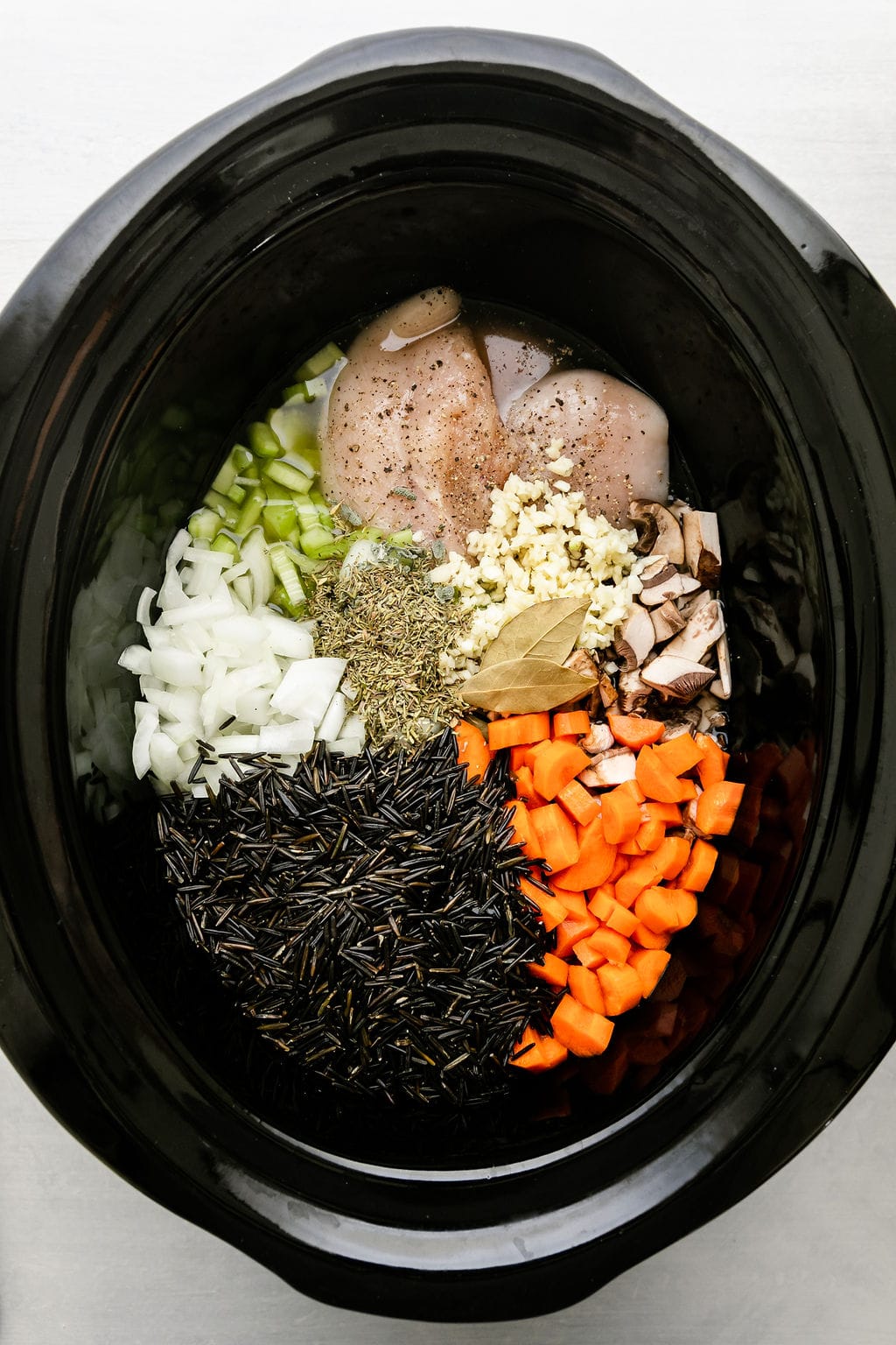 Overhead view black crockpot filled with all ingredients for chicken wild rice soup.