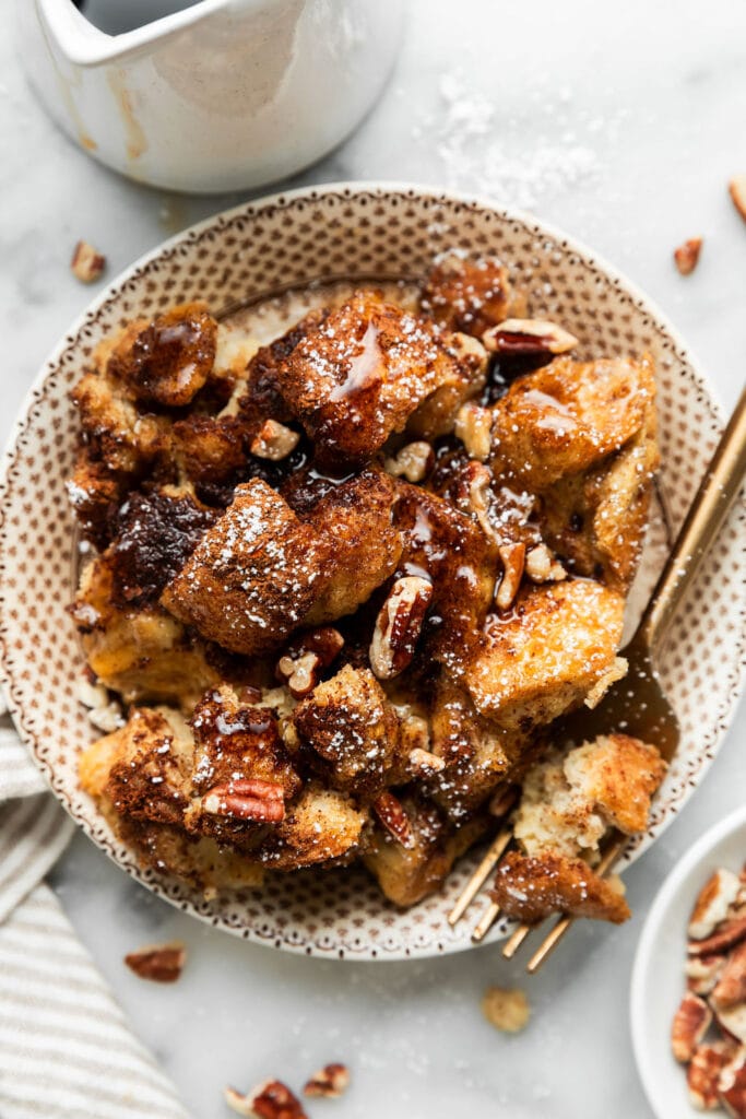 Serving of french toast casserole in bowl topped with pecans and maple syrup