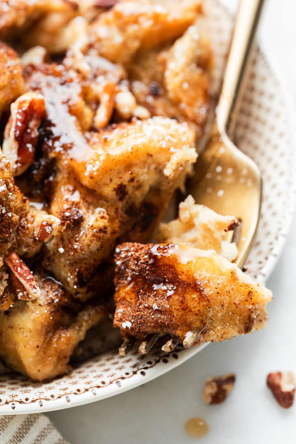 Close up view French toast casserole serving with baked bread pieces coated in maple syrup with powdered sugar and pecans.