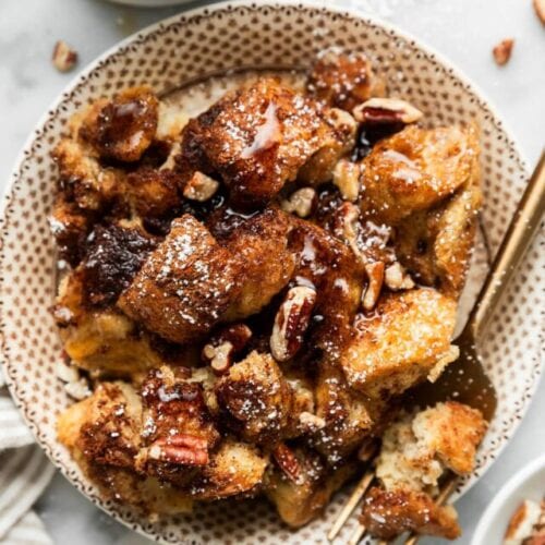 Overhead view serving of crockpot French toast casserole on plate topped with maple syrup and pecans