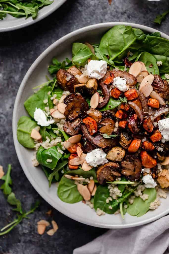Plate filled with bed of spinach and topped with mushrooms, carrots, almonds and goat cheese