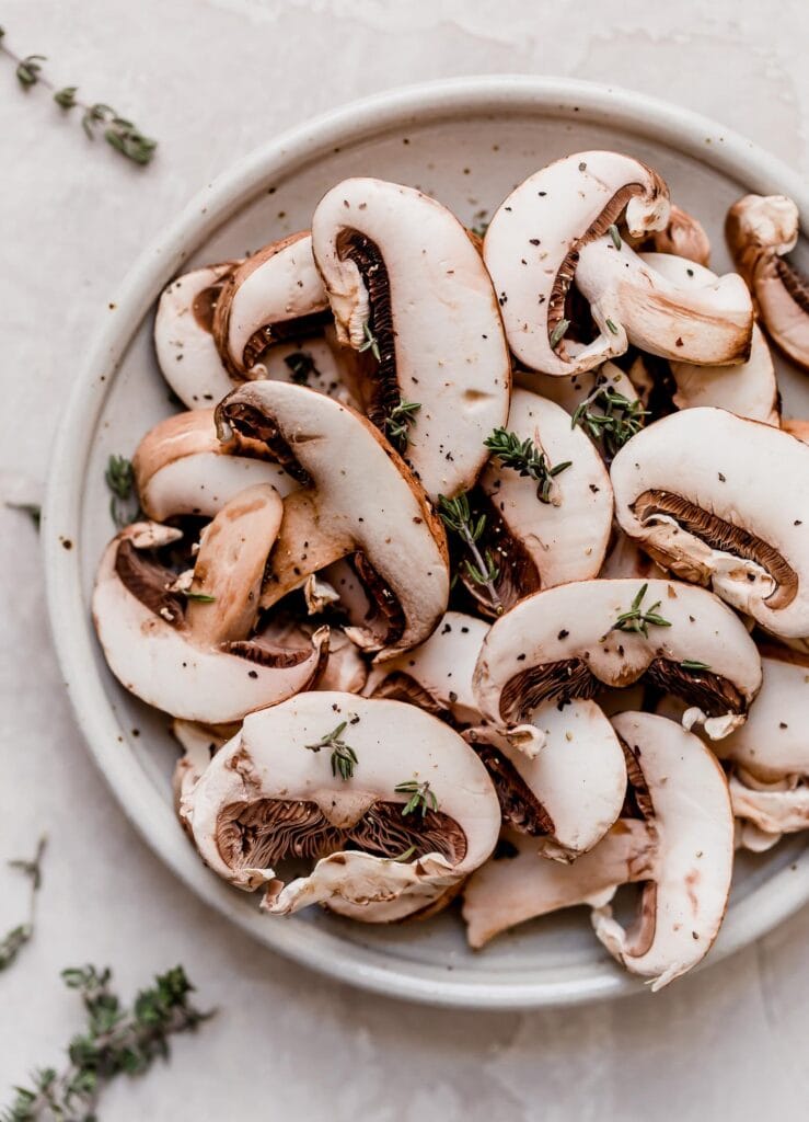 Overhead view fresh sliced mushrooms on small stone plate topped with cracked pepper