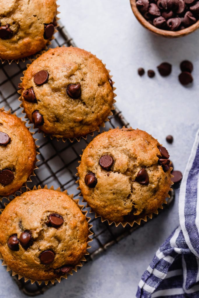 Several banana muffins studded with chocolate chips lined up on a wire cooling rack