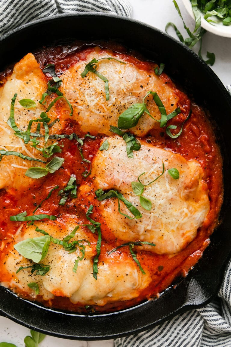 Overhead view of a full recipe of four servings of chicken parmesan in marinara sauce inside of a black cast iron skillet.