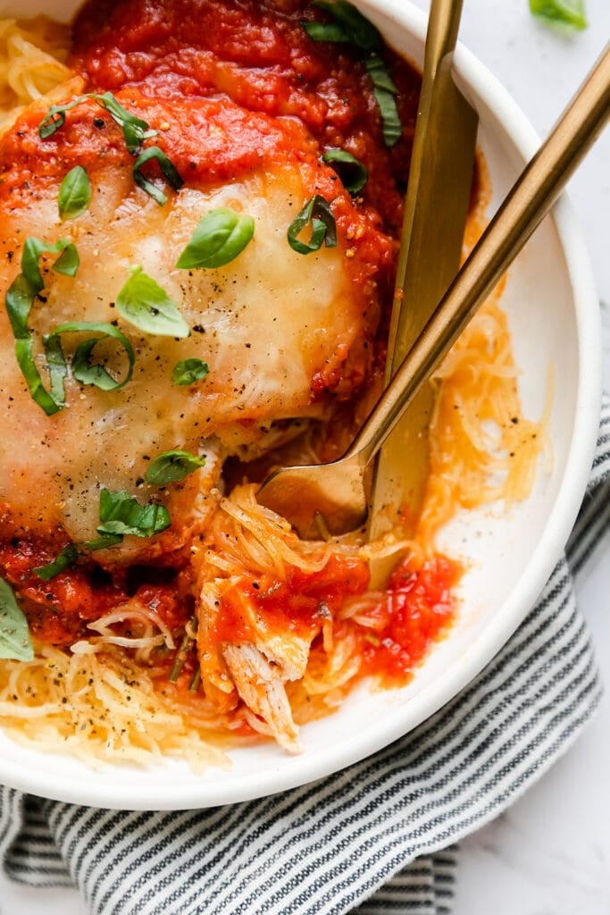 Close up view chicken parmesan served over spaghetti squash strands in white bowl