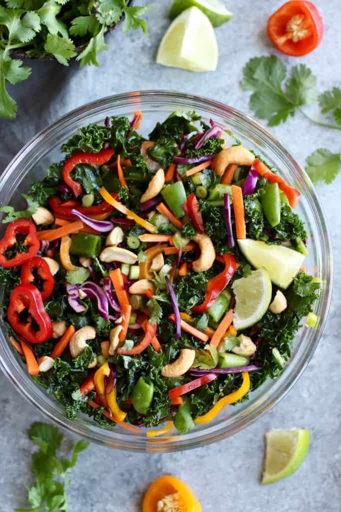 colorful kale salad with peppers, peas and cashews in a glass bowl