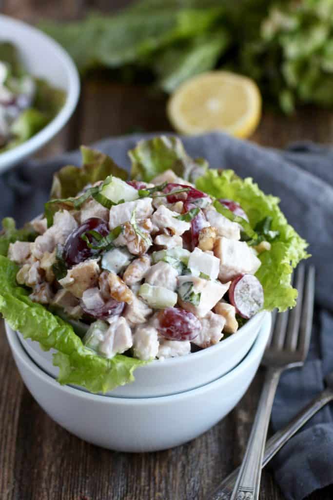 Nested bowls with chicken salad containing walnuts, grapes, celery with lettuce garnish and lemon in the background 