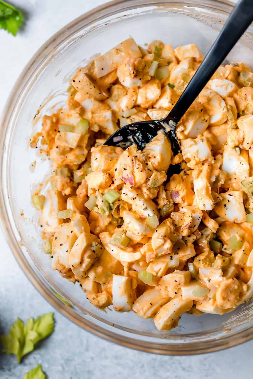 Overhead photo of Buffalo Ranch Egg Salad in a clear bowl with a black spoon. 