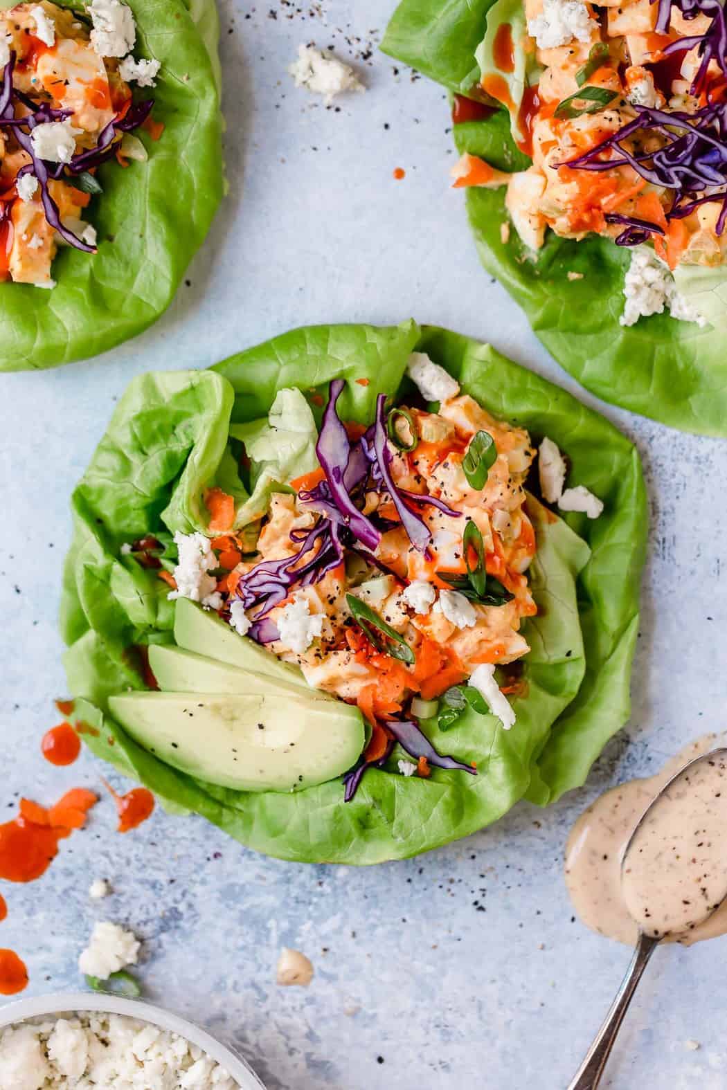 Photo of Buffalo Ranch Egg Salad in a butter lettuce leaf with avocado slice and topped with shredded red cabbage, shredded carrots, green onion slices and crumbled blue cheese.