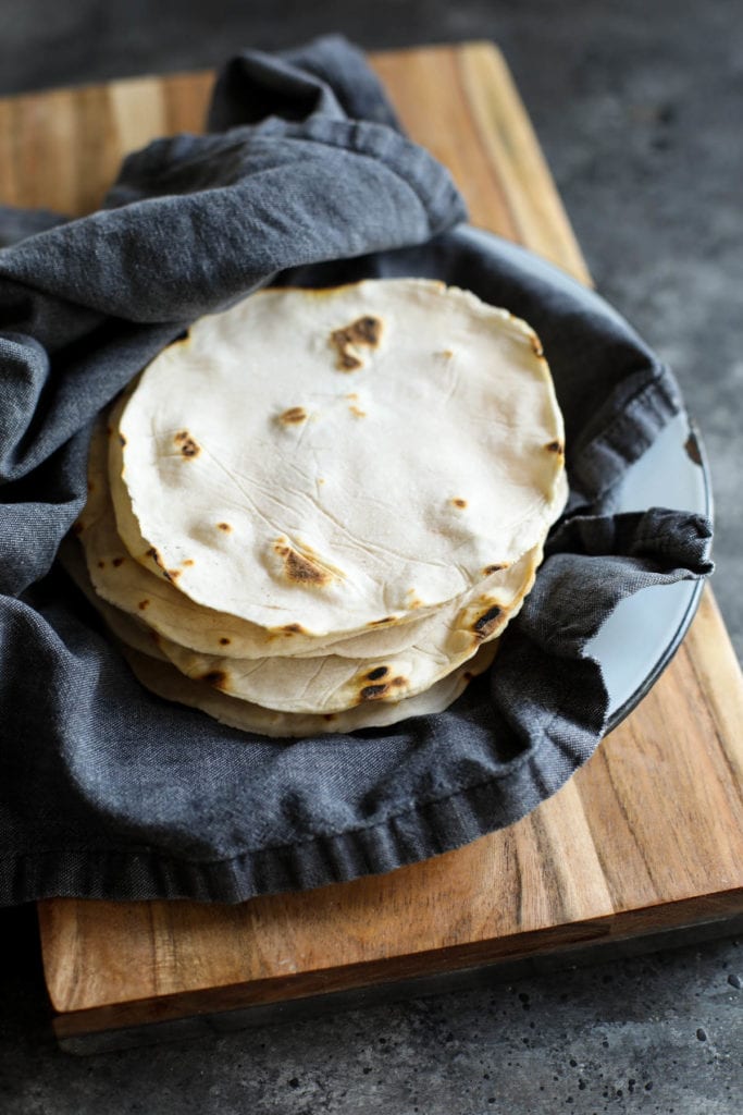 Napkin-lined basket with grain-free tortillas resting on a wooden cutting board