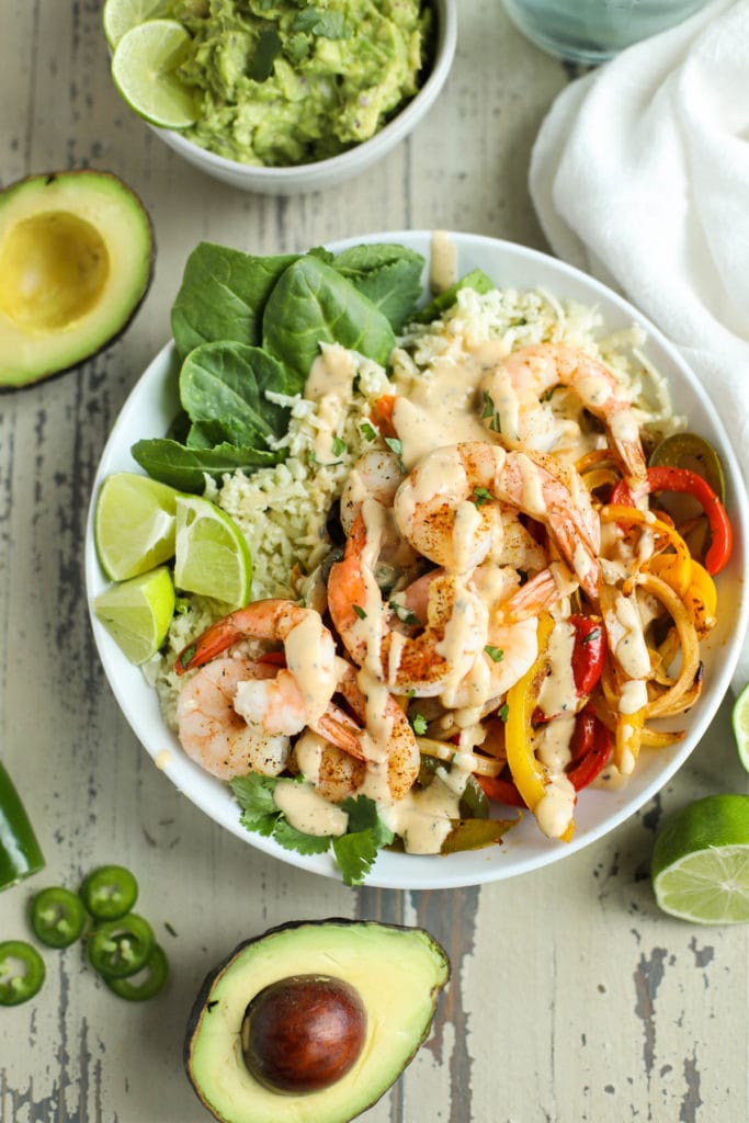 Overhead view of a plate of shrimp fajitas and rice, topped with a creamy salsa ranch and fresh cilantro. 