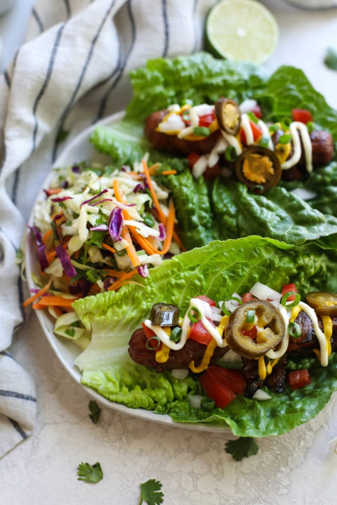 Three grilled hot dogs topped with slaw in lettuce leaves with lime garnish