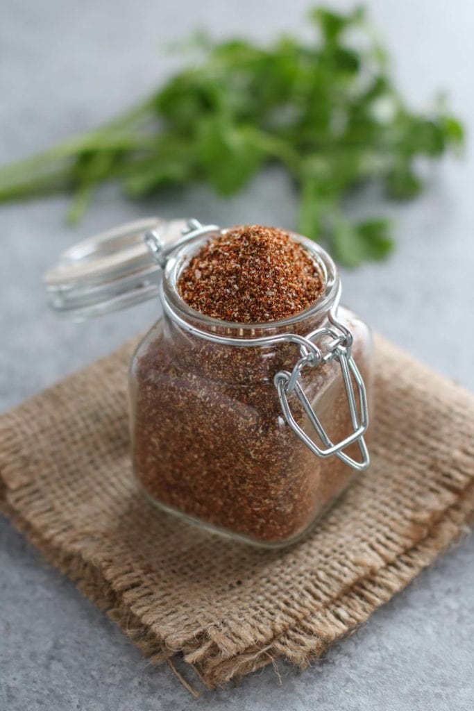 Small glass jar filled with taco seasoning resting a square of burlap