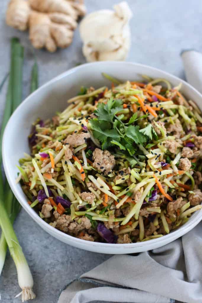 Bowl filled with broccoli and cabbage slaw and ground meat with a cilantro garnish resting on napkin.