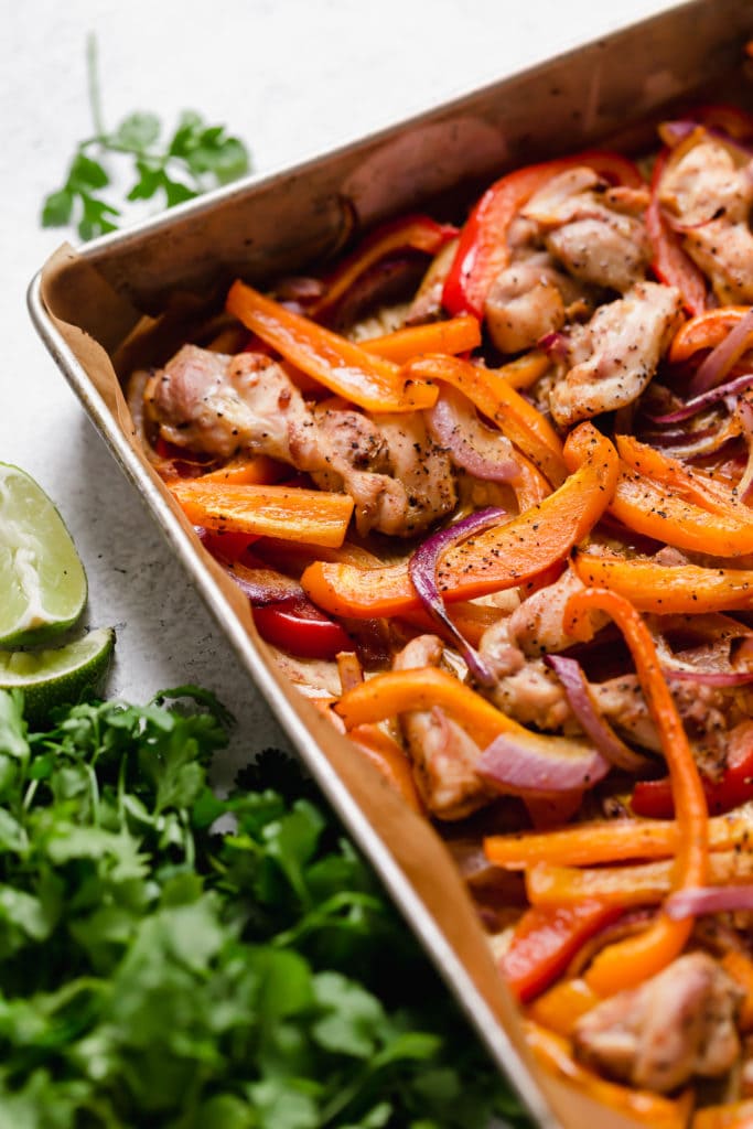 Pan of baked chicken, peppers, onions with cilantro and lime garnish