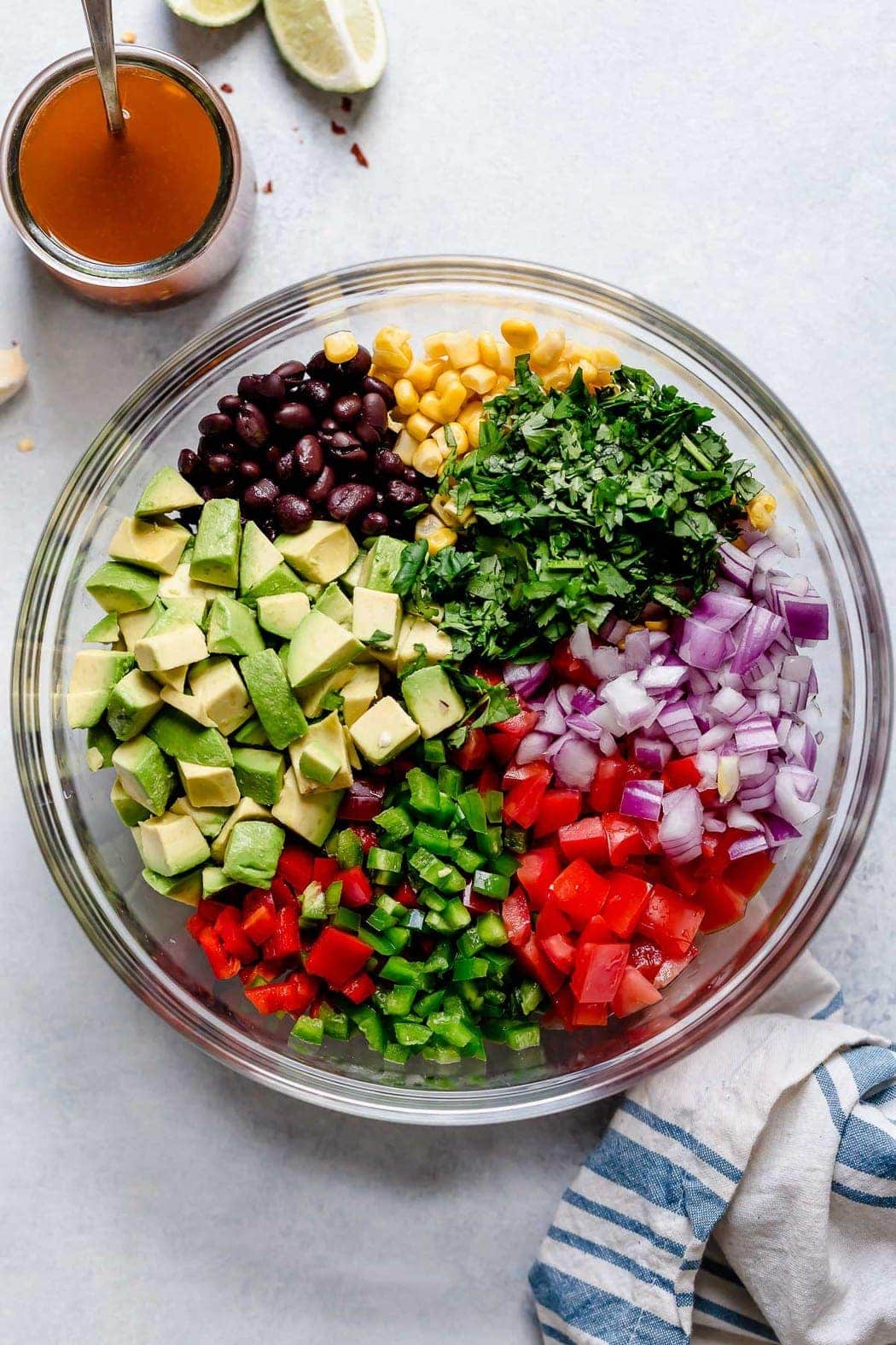 All ingredients for black bean and corn salsa arranged in a clear glass mixing bowl ready to be tossed together. 