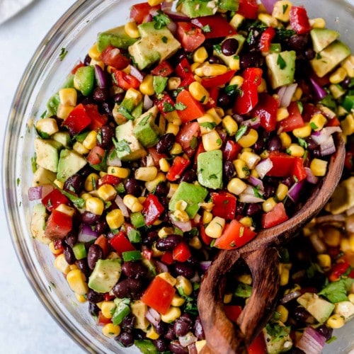 Black bean and corn salsa with avocado mixed together with chili lime vinaigrette in a clear glass mixing bowl.