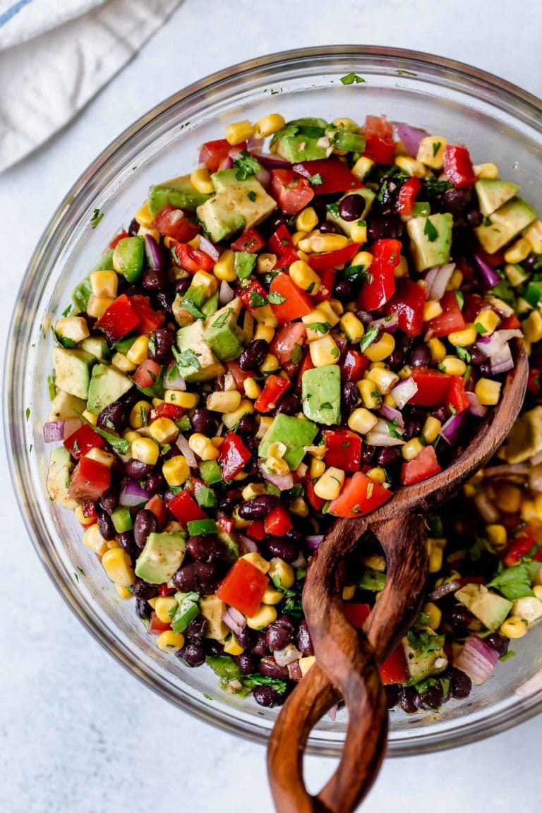 Black bean and corn salsa with avocado mixed together with chili lime vinaigrette in a clear glass mixing bowl.