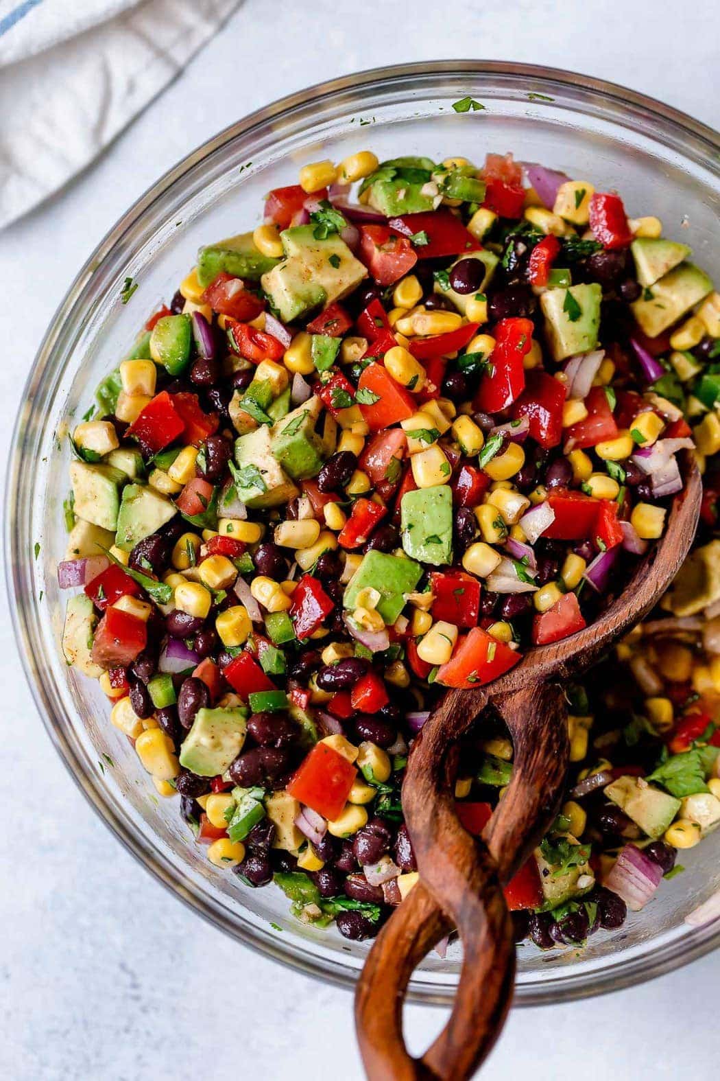 Black bean and corn salsa with avocado mixed together with homemade sauce in a clear glass mixing bowl. 